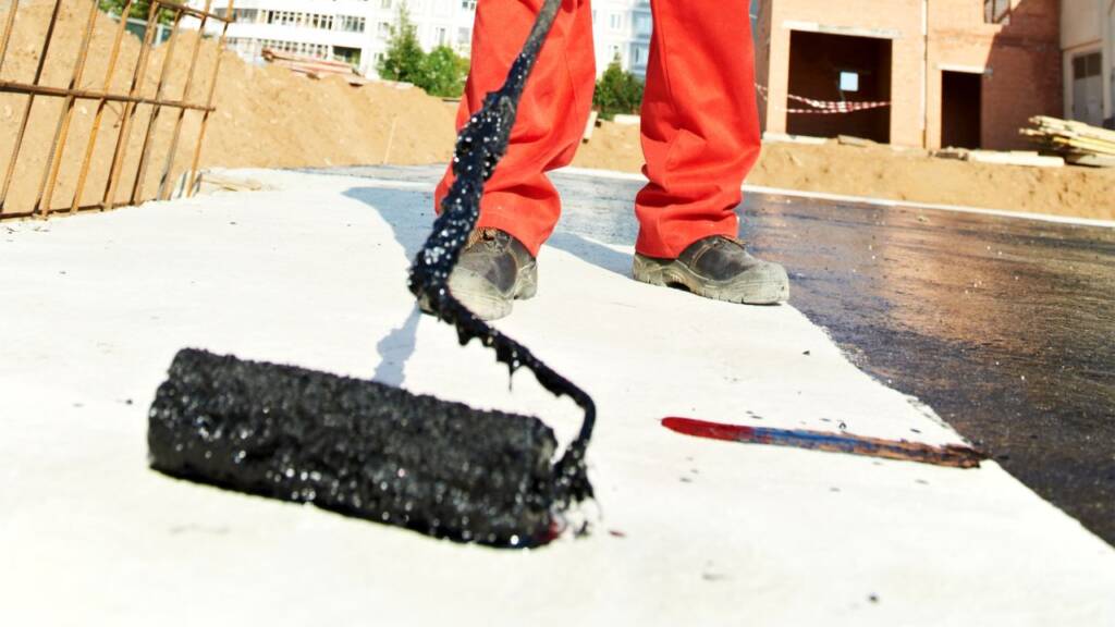 Pracownik budowlany malujący dach czarną masą bitumiczną